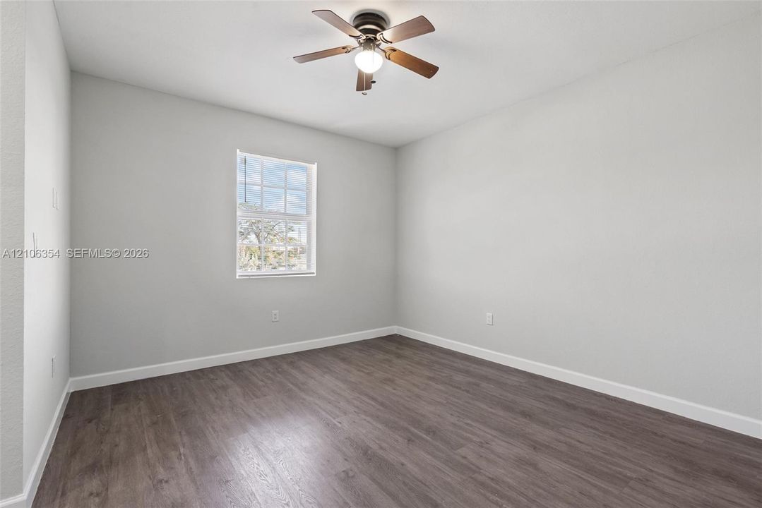 Room featuring wood-finish flooring, a single-hung window with grid detailing, and a ceiling-mounted light fixture with a fan