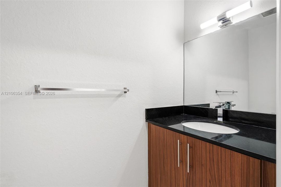 Vanity featuring a dark stone countertop, integrated oval basin, horizontal wood-finish cabinetry, a full-width mirror, and a linear wall-mounted light fixture