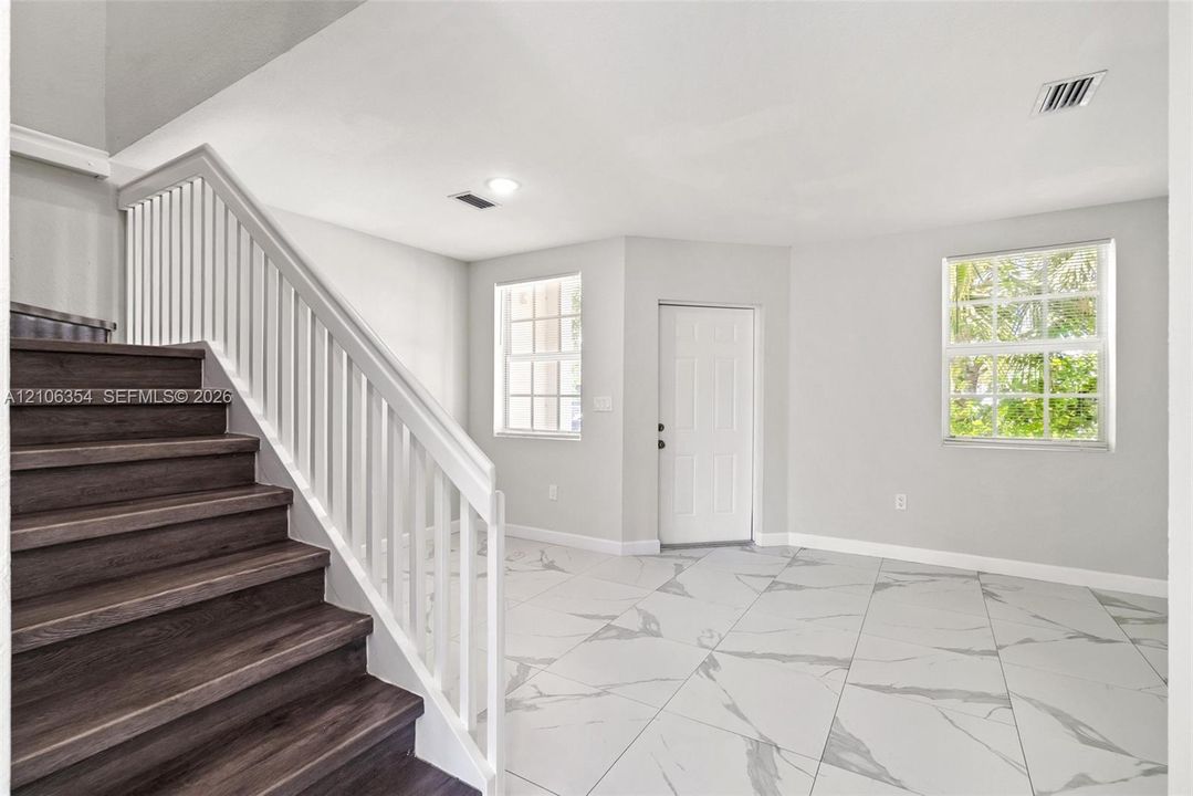 Foyer featuring large-format tile flooring, a staircase with wood-finish treads, and a white balustrade railing