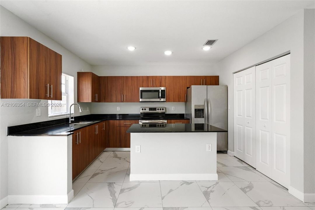 Kitchen featuring wood-finish cabinetry, black stone countertops, a central island, stainless steel appliances, and large-format tile flooring