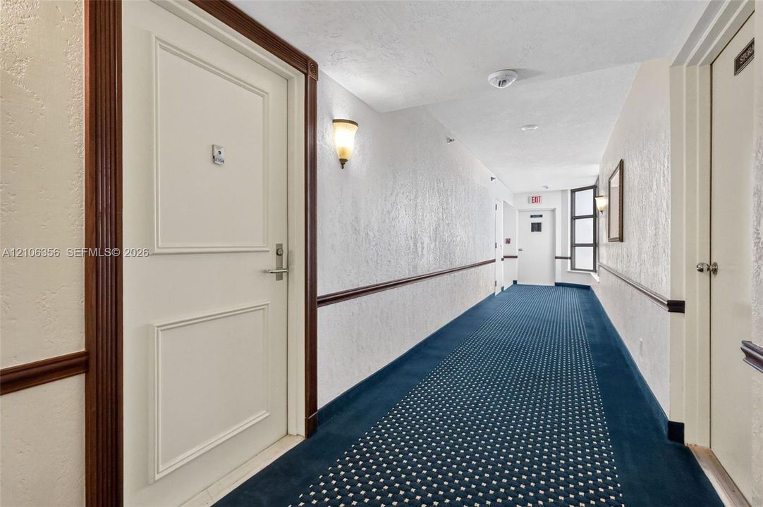 Hallway featuring patterned carpeting, paneled interior doors, wood-finish door casing and chair rail, and wall-mounted sconce lighting