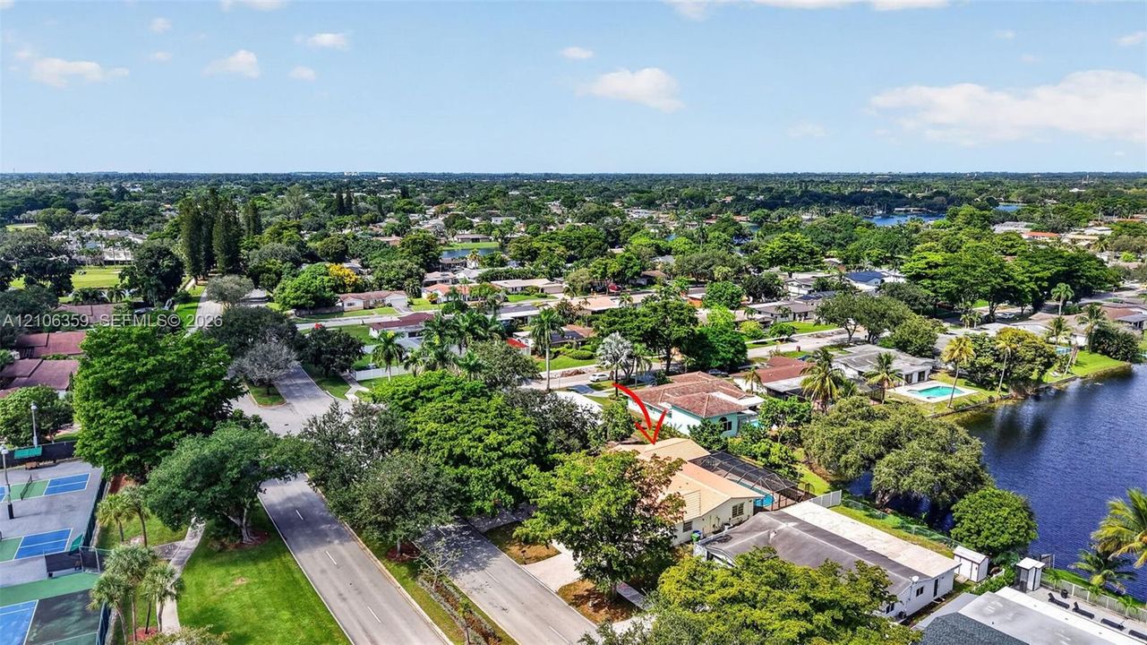Aerial perspective featuring proximity to a waterfront area, established trees, and hard-surfaced recreational courts