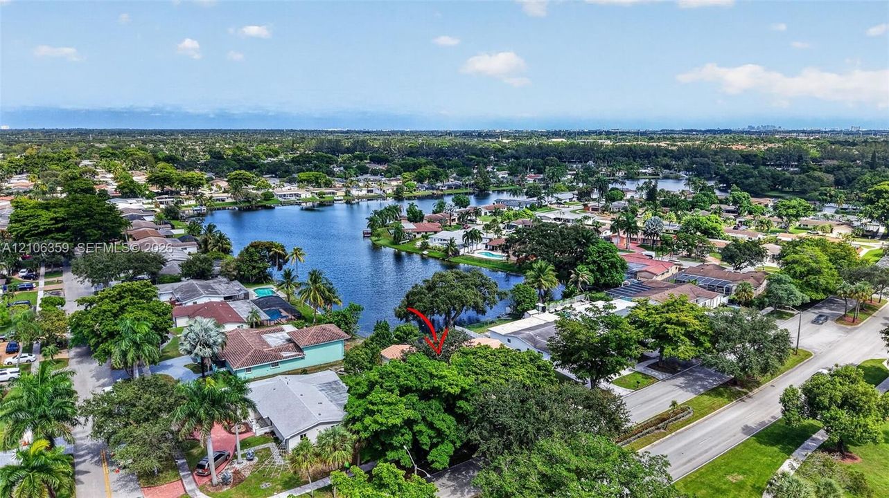 Aerial perspective featuring mature trees, a multi-pitched roofline, and proximity to a large body of water