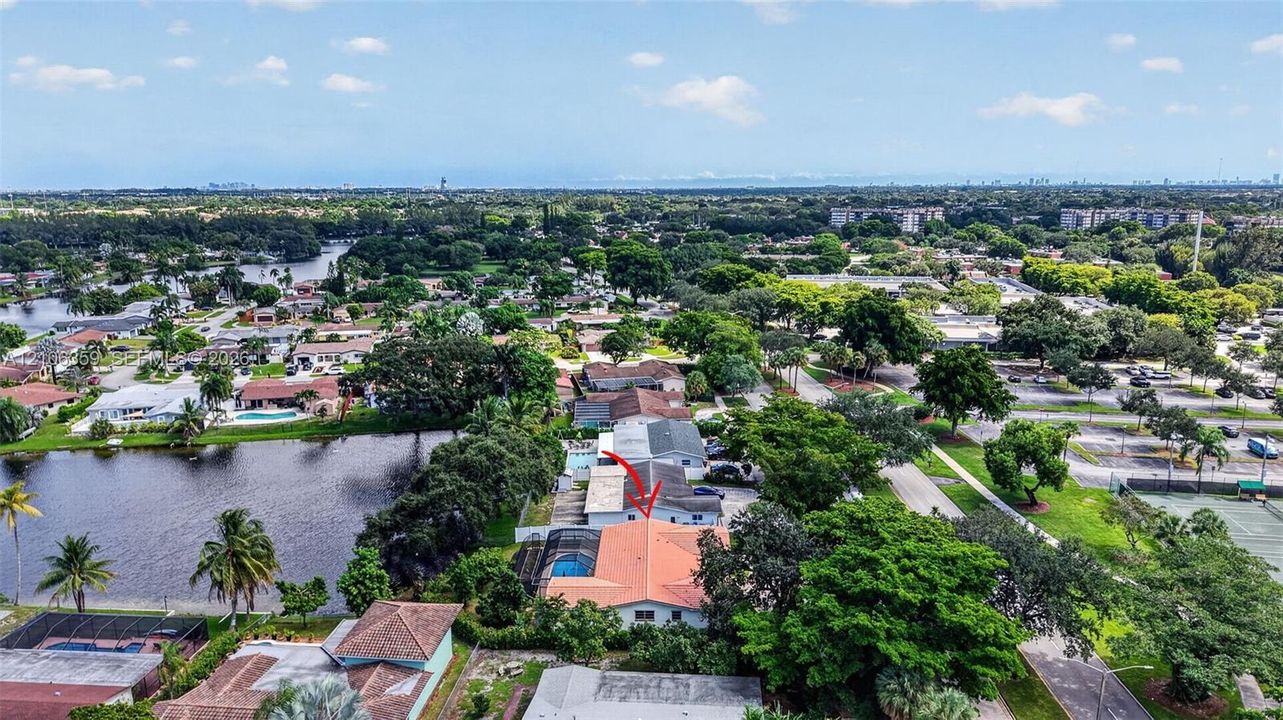Aerial perspective featuring a single-story residence with a multi-hipped tile roof, a screened-in lanai, and a private swimming pool, situated on a waterfront lot with mature canopy trees