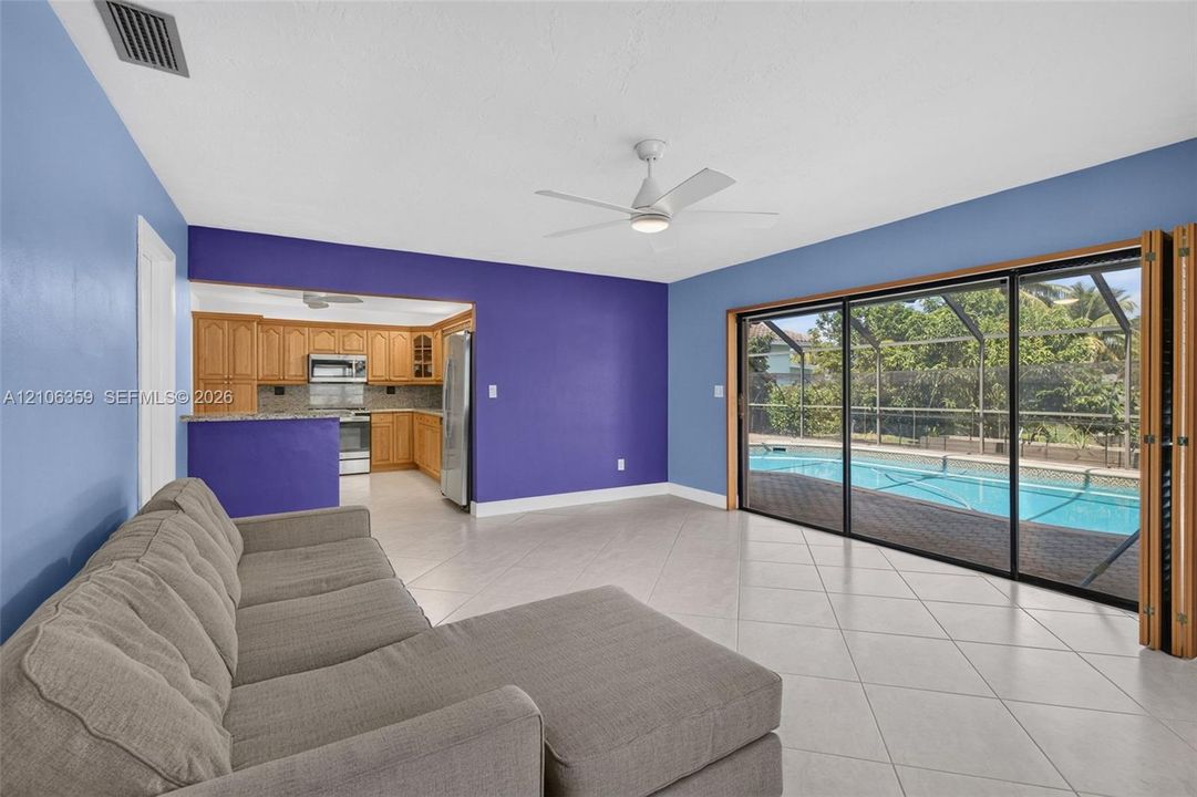 Open-concept living space featuring large-format ceramic tile flooring, a white ceiling fan, multi-panel sliding glass doors, and a screen-enclosed pool