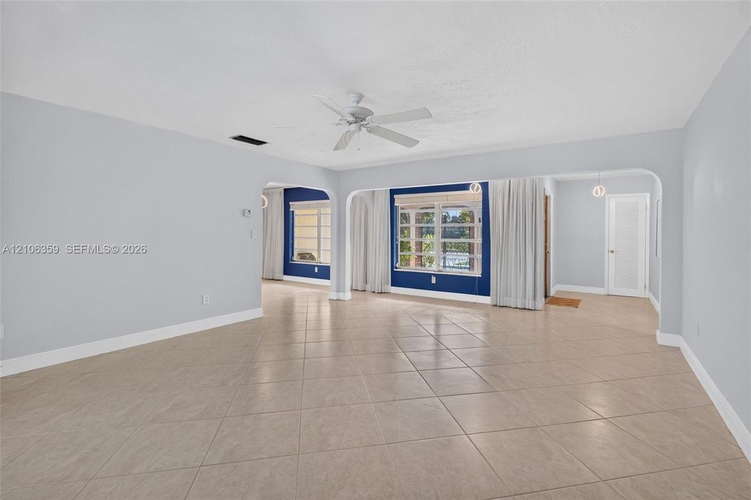 Open interior featuring large-format tile flooring, arched structural openings, a ceiling fan, and multi-pane windows
