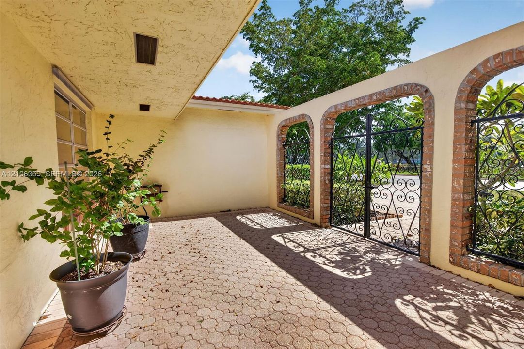 Covered courtyard featuring paver flooring, stucco wall finish, and decorative brick-trimmed archways with custom wrought iron gates