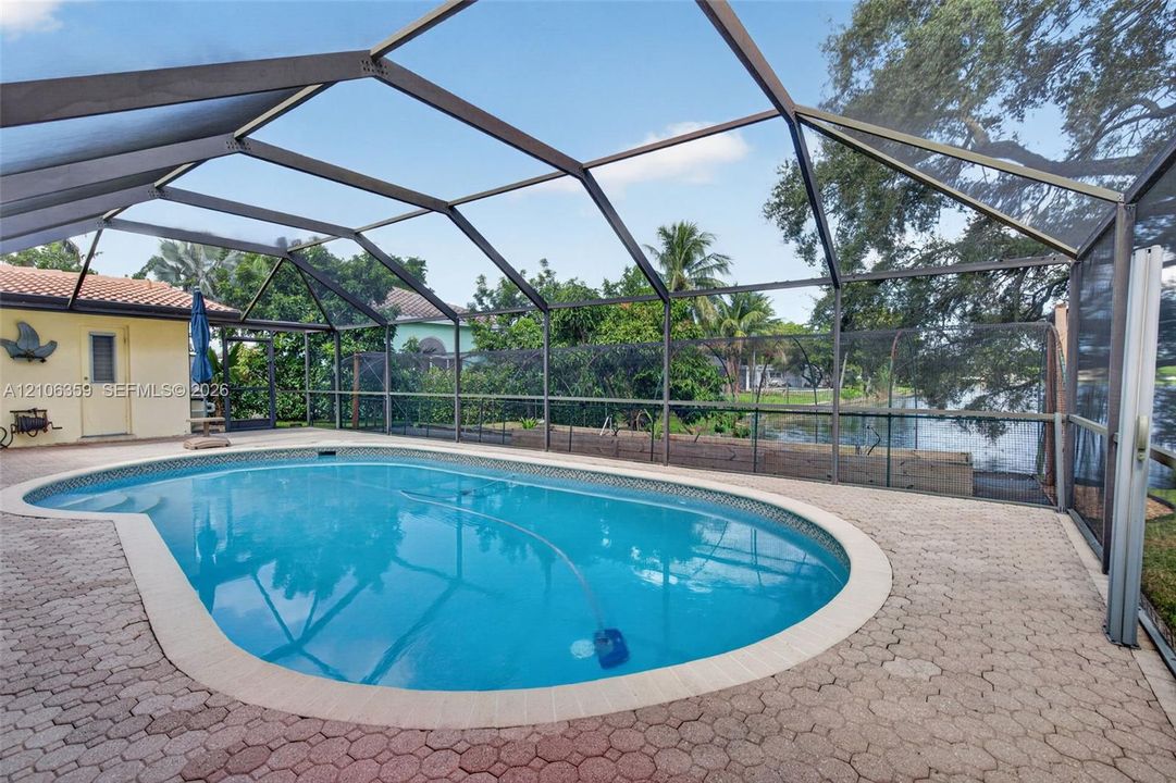 Screened-in patio area featuring a concrete paver pool deck, a kidney-shaped inground pool, and direct water frontage