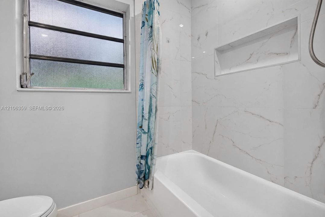 Bathroom featuring a full-length tub with stone-finish wall tile, an integrated recessed wall niche, and a window with privacy glass