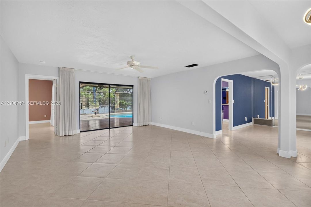 Open-concept interior featuring large-format tile flooring, arched wall openings, a ceiling fan, and sliding glass doors with exterior pool access