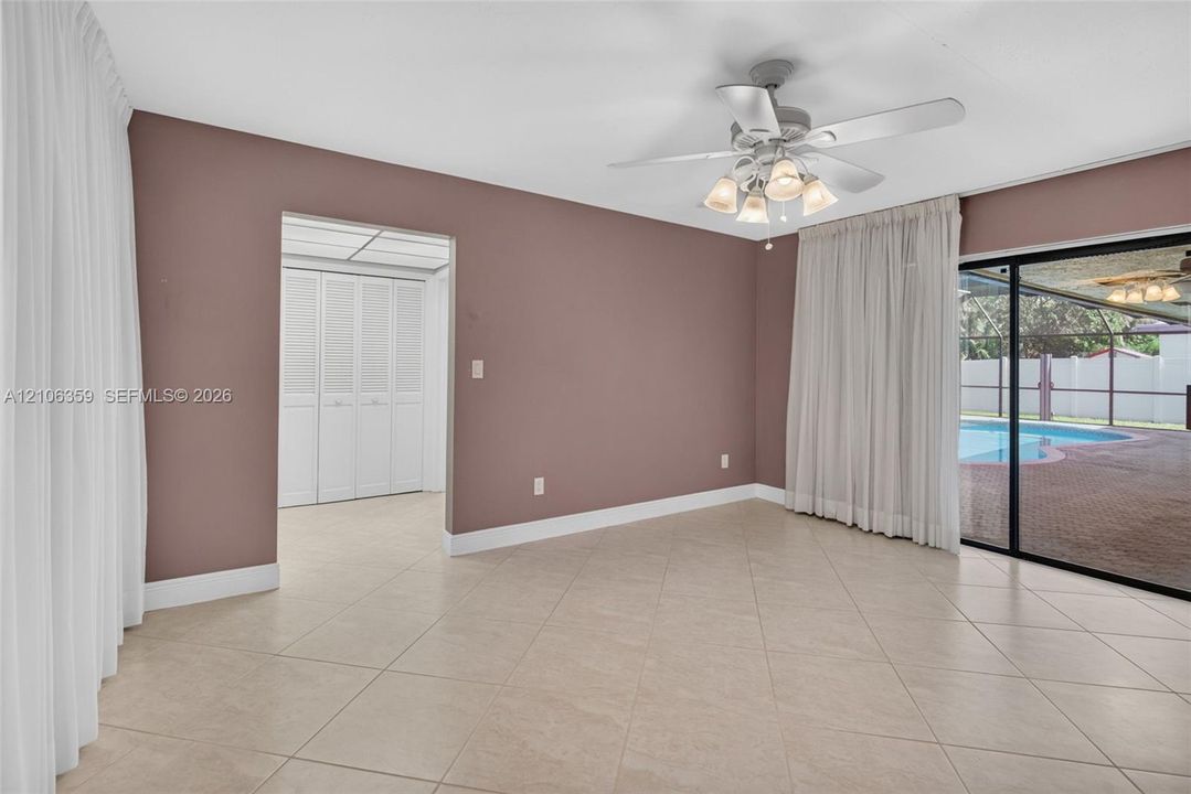 Spacious interior featuring large-format tile flooring, a multi-light ceiling fan, sliding glass doors, and louvered closet doors