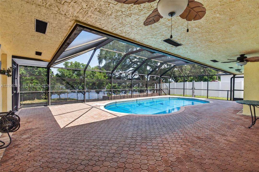 Screened lanai featuring a paved deck, built-in ceiling fans, a swimming pool, and a perimeter fence