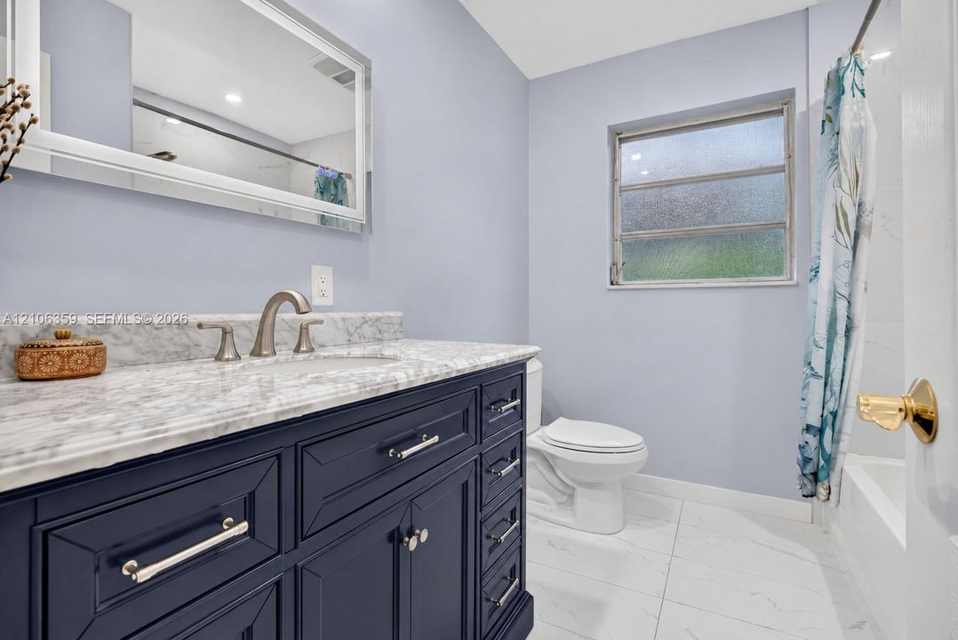 Bathroom featuring a designer vanity with polished stone countertop, undermount sink, brushed-nickel faucet, and large-format tile flooring