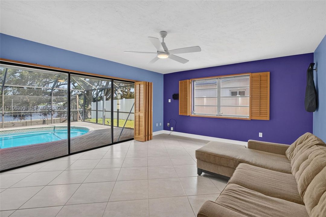 Living area featuring ceramic tile flooring, a multi-blade ceiling fan with integrated lighting, and wooden interior shutters