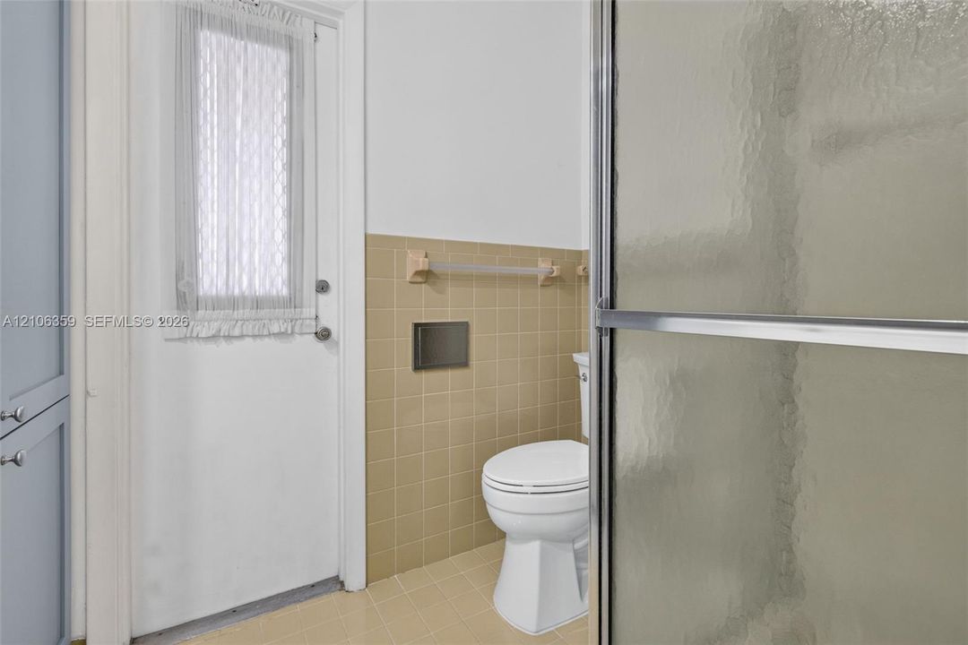 Full-height cabinetry, glass-enclosed shower, light-toned ceramic wall and floor tiling, and a dedicated entry door with integrated window