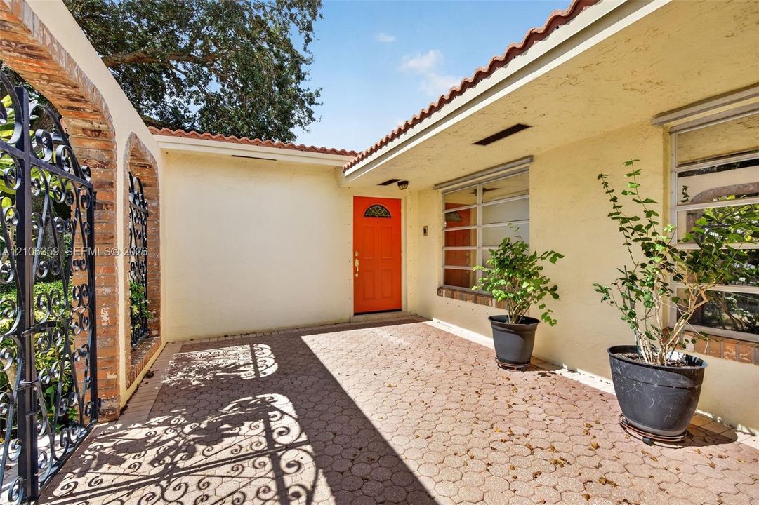Private courtyard entrance featuring geometric stone pavers, a decorative iron gate, arched brick entry accents, and a tile roof