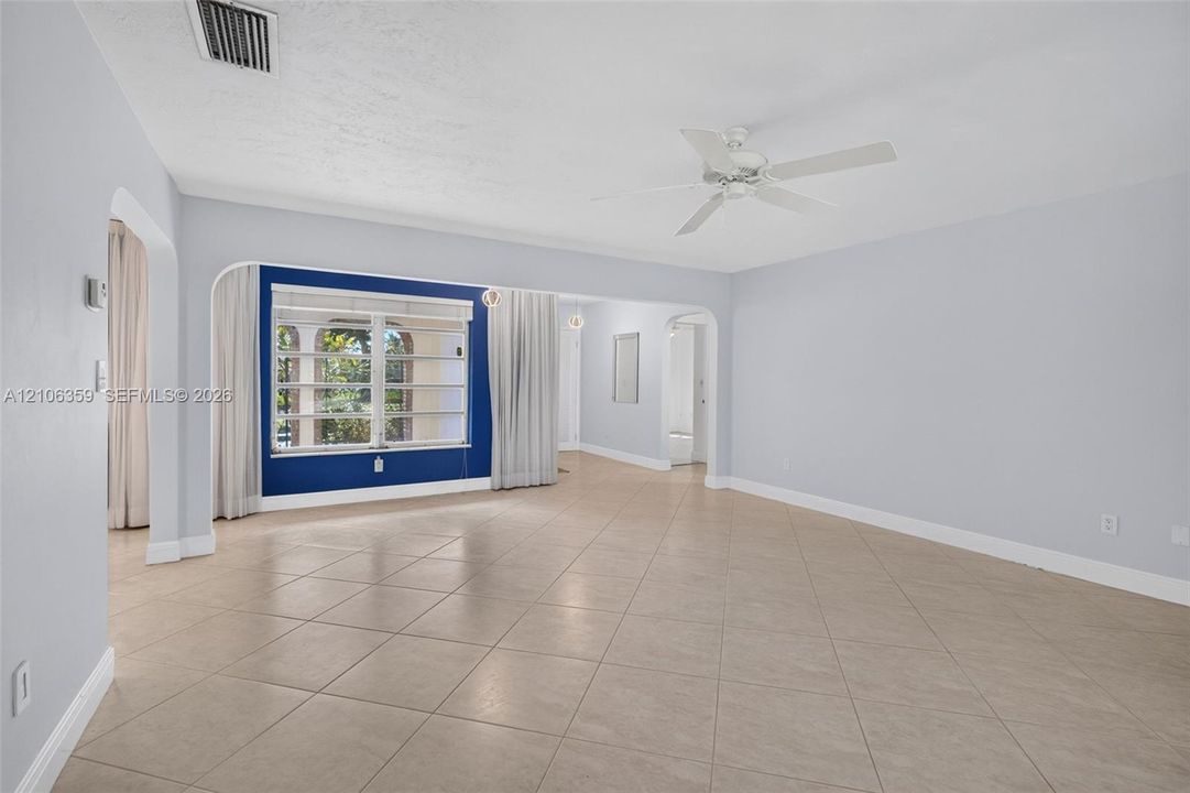 Spacious room featuring neutral ceramic tile flooring, arched entryways, a white ceiling fan, and large windows with horizontal blinds