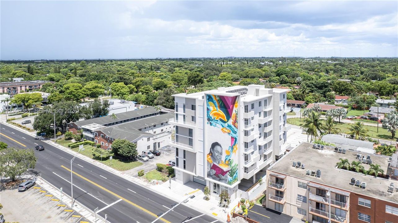 Multi-story mid-rise building featuring a prominent exterior mural, stacked balconies, and paved surface parking