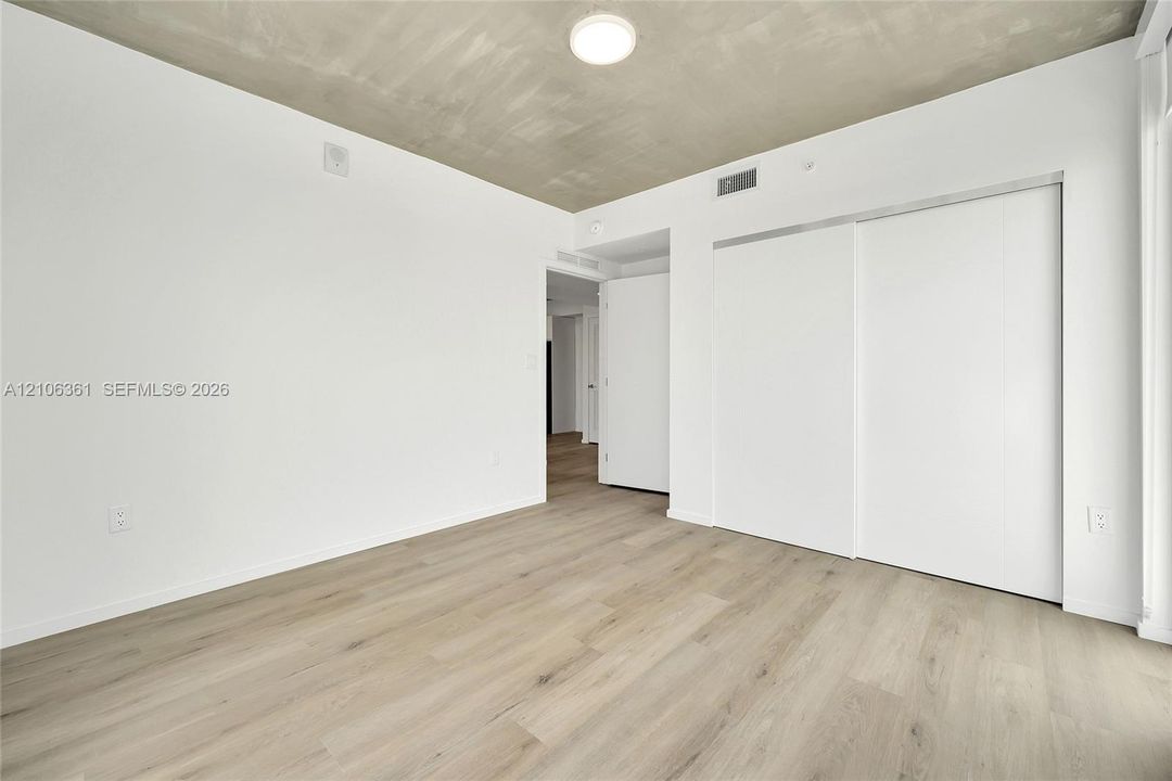 Room featuring high-contrast exposed concrete ceiling, wood-finish flooring, white walls, and built-in sliding door closet with polished hardware