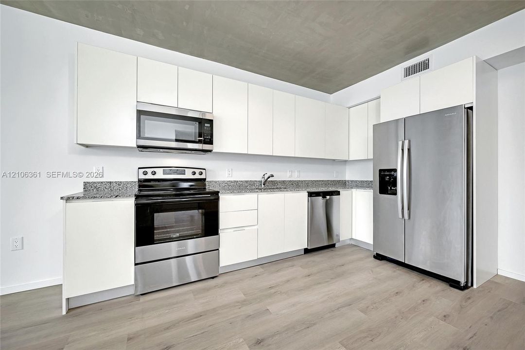 Kitchen featuring sleek white cabinetry, stone-finish countertops, stainless steel appliances, and wood-finish flooring under a concrete ceiling