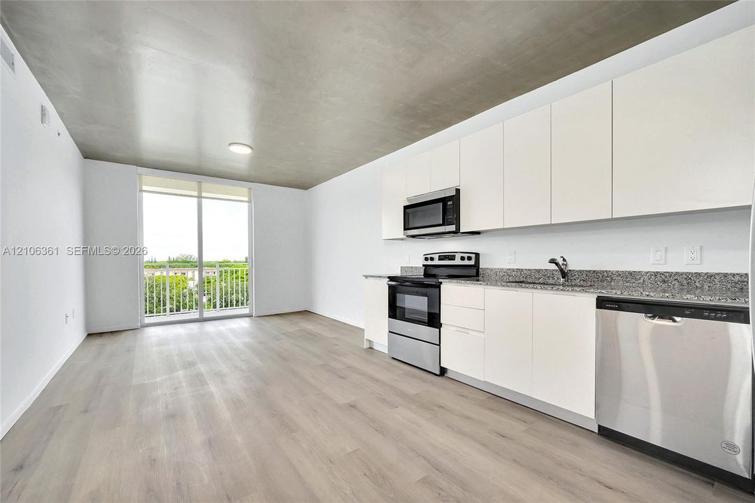 Kitchen featuring flat-panel cabinetry, stone countertops, stainless steel appliances, wood-finish flooring, and a sliding glass door