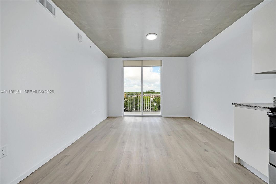 Modern living space featuring an exposed concrete ceiling, wood-finish flooring, sliding glass doors to a private balcony, and sleek cabinetry