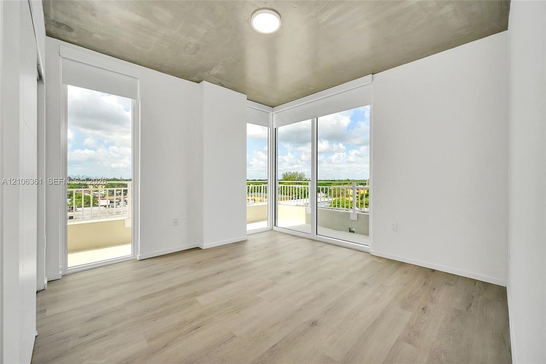 Room with wood-finish flooring, exposed concrete ceiling, flush-mount lighting, and dual glass door access to an exterior terrace with a metal railing