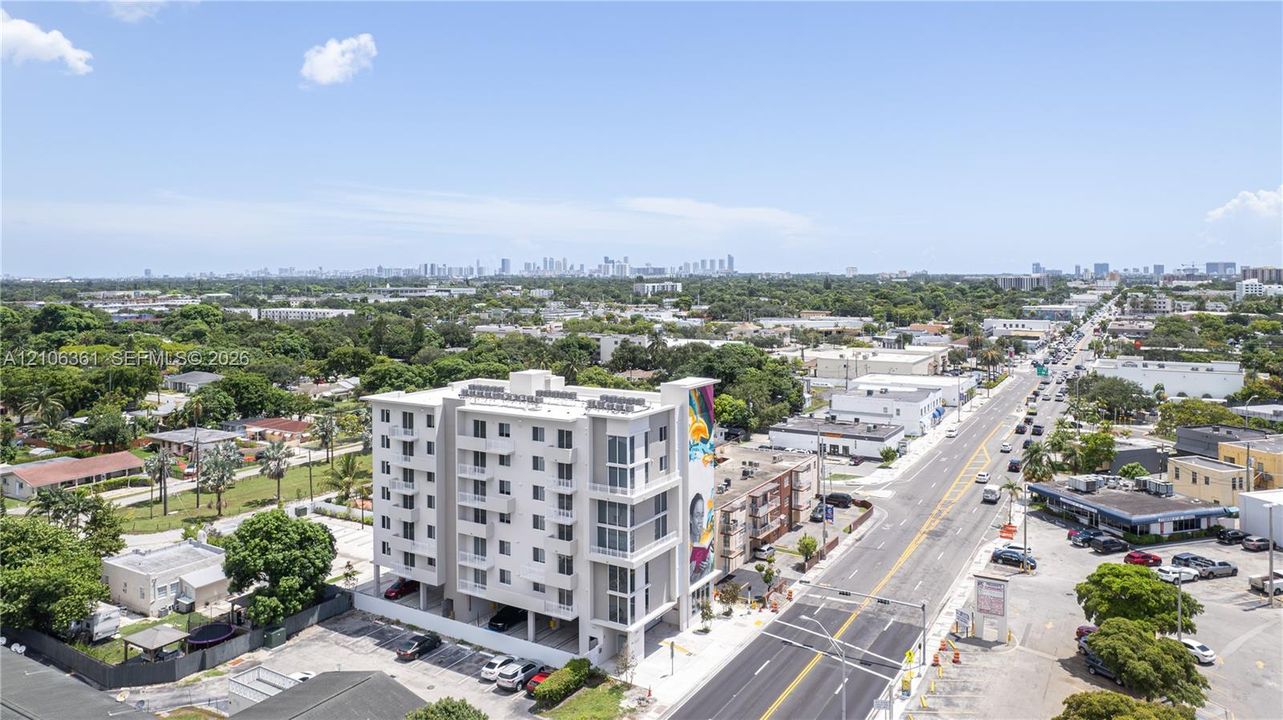 Mid-rise residential building featuring multi-level balconies, ground-level parking, and a prominent exterior mural