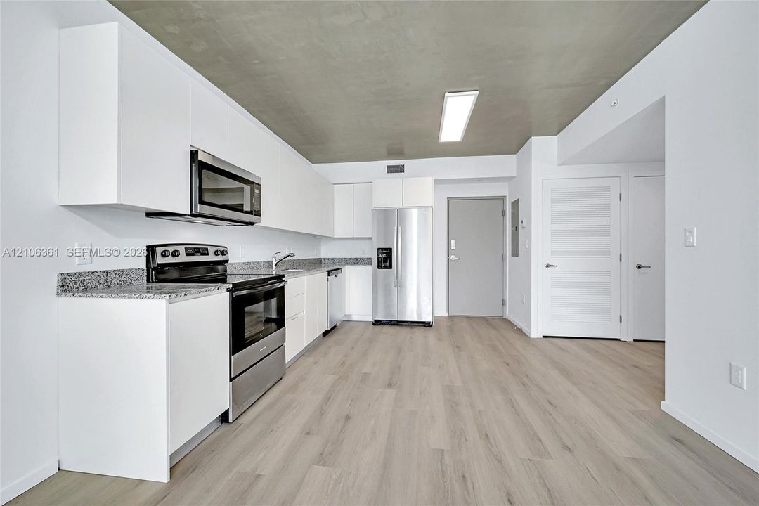 Kitchen featuring white flat-panel cabinetry, stone-finish countertops, stainless steel appliances, and wood-finish flooring under a concrete-texture ceiling