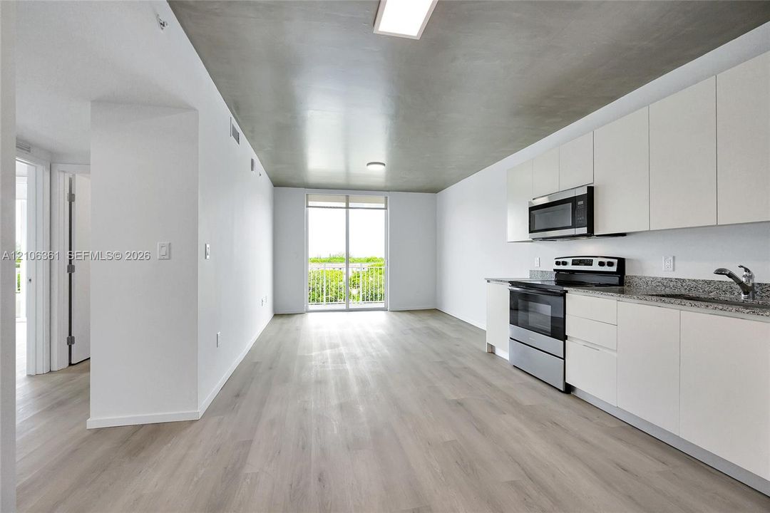 Modern kitchen area featuring flat-panel cabinetry, stone countertops, stainless steel appliances, wood-finish flooring, and a concrete-texture ceiling
