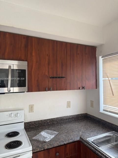 Kitchen featuring dark wood-finish cabinetry, stainless steel microwave, stone-patterned laminate countertops, and an integrated stainless steel sink