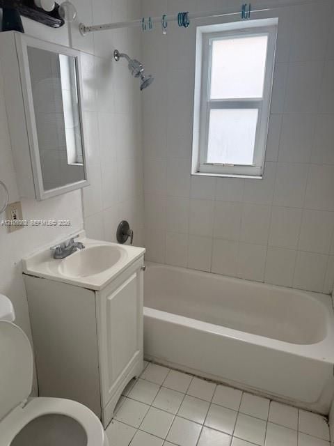 Bathroom featuring a white pedestal vanity with an integrated sink, porcelain tile wall surround, built-in medicine cabinet, and a bathtub with a shower fixture