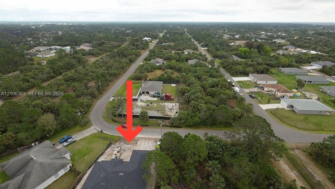Aerial perspective of a corner lot featuring a dark shingle roof, concrete driveway, and established surrounding vegetation