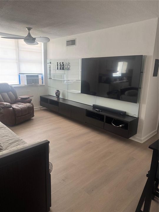 Wall-mounted dark wood-finish cabinetry, floor-to-ceiling glass paneling, light wood-finish flooring, and a modern ceiling fan