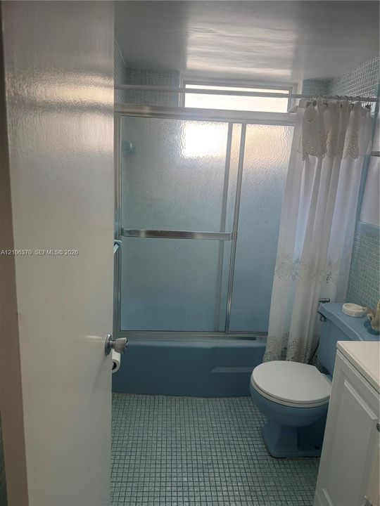 Bathroom featuring a combination bathtub and shower with a sliding glass enclosure, mosaic-tiled walls, grid-patterned floor tiling, and a vanity cabinet