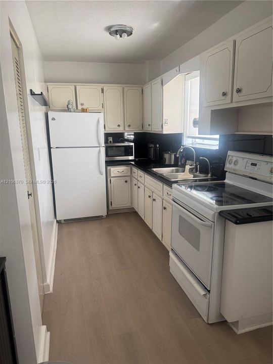 Kitchen featuring white cabinetry, wood-finish flooring, dark solid-surface countertops, dual-basin stainless steel sink, and white appliances