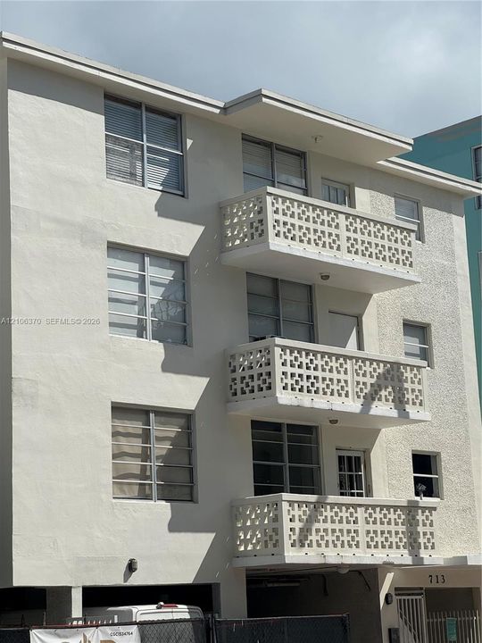 Multi-level exterior facade featuring a smooth stucco finish, grid-patterned privacy screens on each balcony, and horizontal sliding windows