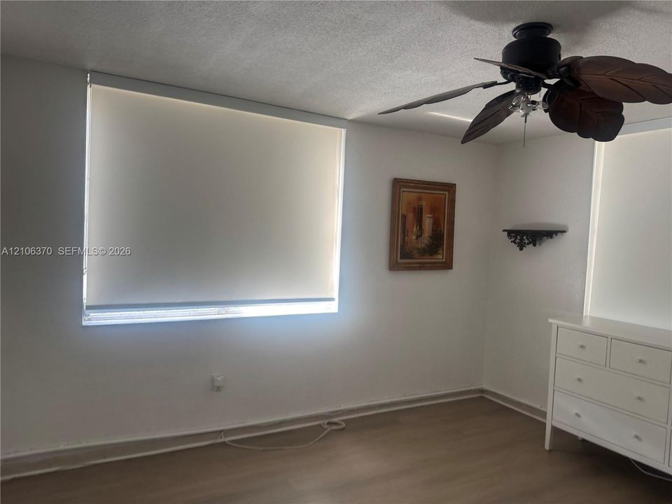 Room featuring wood-finish flooring, dual windows with roller shades, and a ceiling fan with leaf-style blades