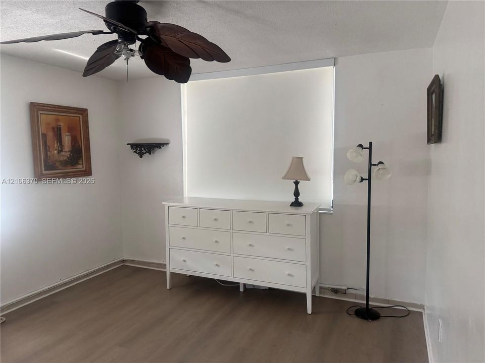 Wood-finish flooring, ceiling fan with leaf-style blades, and a wall-mounted decorative shelf