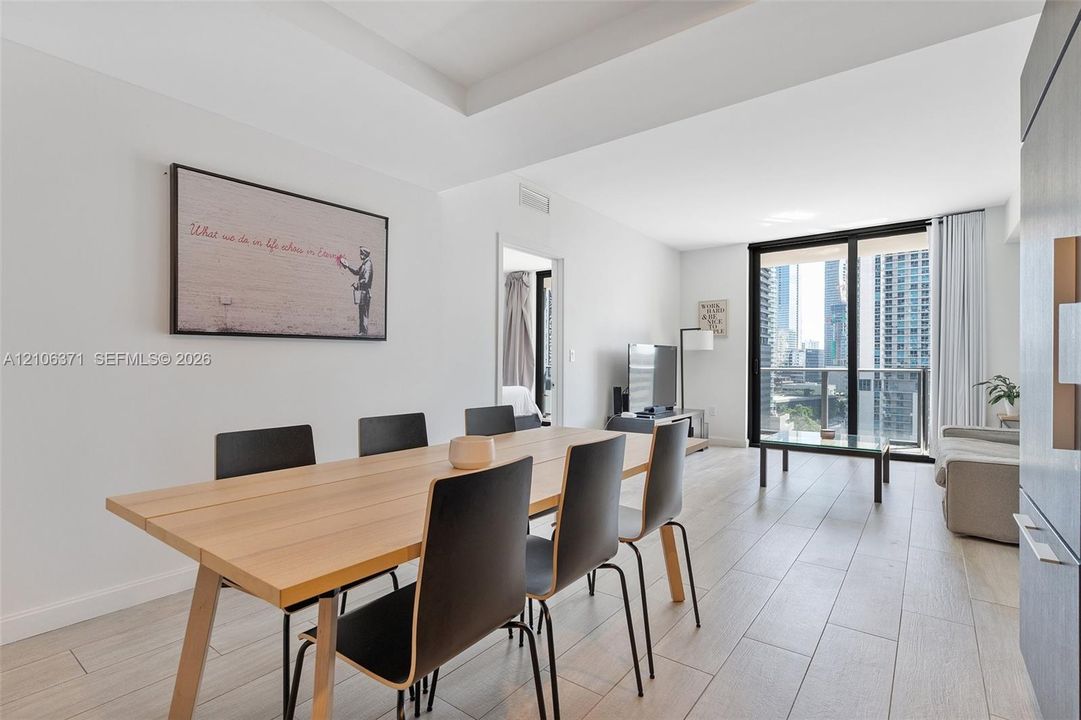 Living space featuring wood-finish tile flooring, recessed tray ceiling, and floor-to-ceiling glass sliding doors opening to a balcony