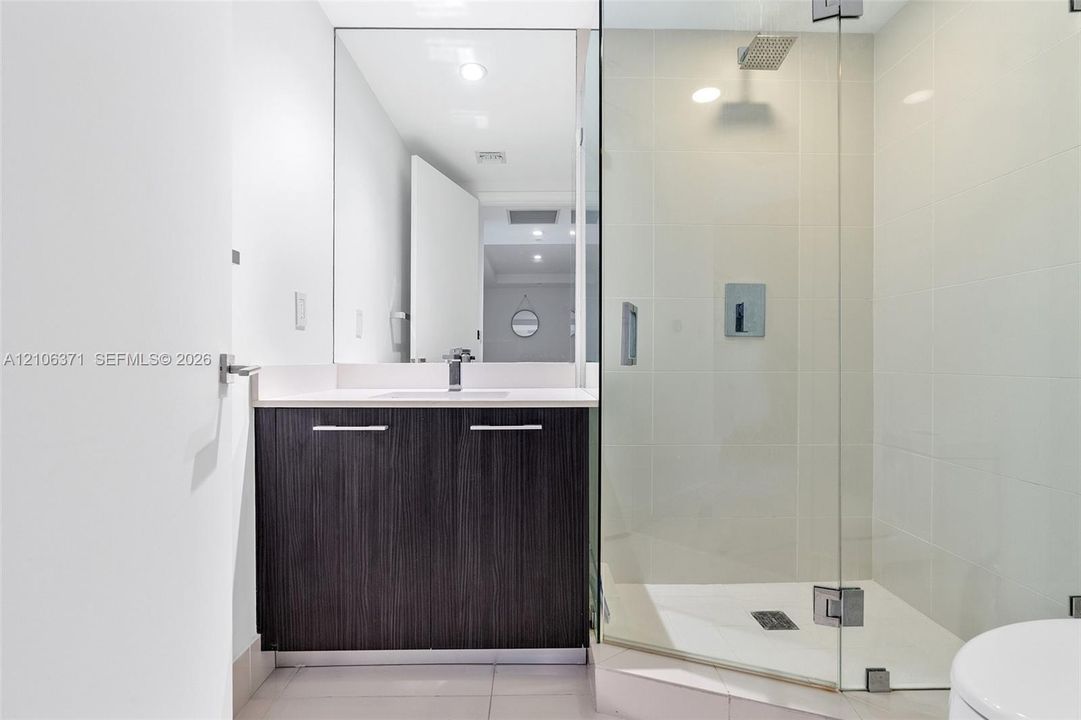 Modern bathroom featuring a dark wood-finish dual-vanity with chrome hardware, white quartz countertop, and an illuminated mirror