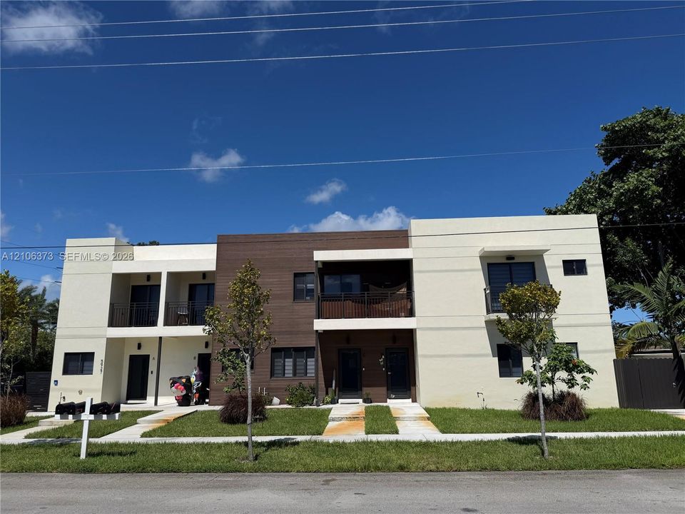 Contemporary two-story exterior featuring multi-textured facade, wood-finish paneling, private balconies with metal railings, and concrete walkways
