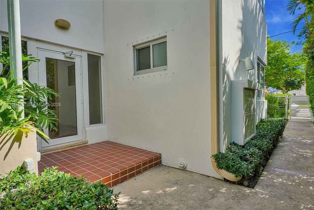 Exterior entrance featuring a tiled stoop, stucco facade, glass-paneled entry door, and wall-mounted exterior lighting