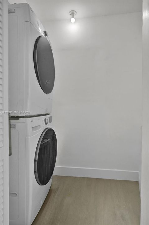 Utility area featuring a stacked washer and dryer unit, light-toned wood-finish flooring, and a ceiling-mounted light fixture