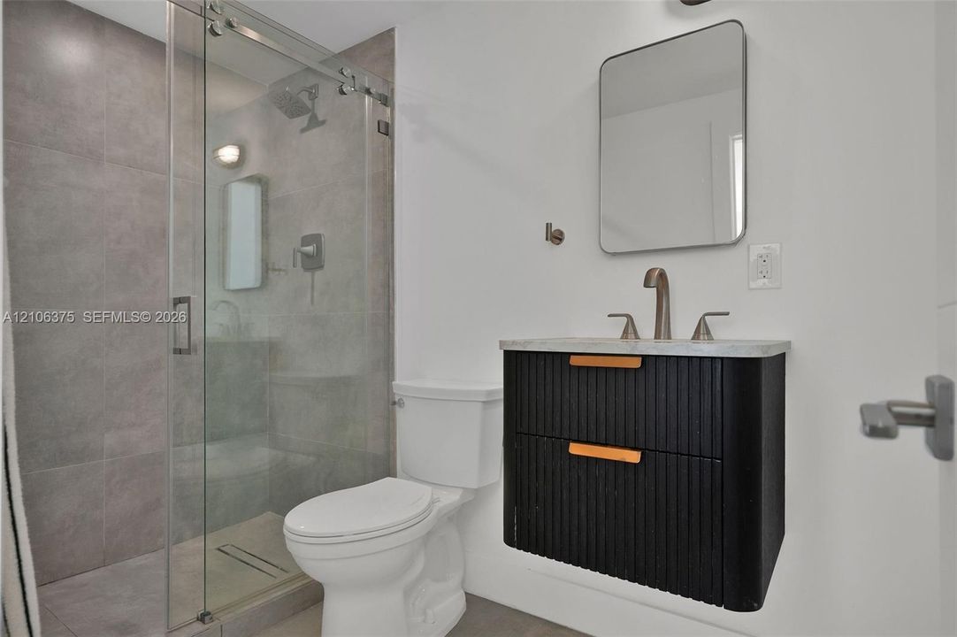 Floating ribbed vanity with stone countertop, walk-in shower with glass enclosure and neutral-toned wall tile, rectangular wall-mounted mirror, and metal faucet fixtures