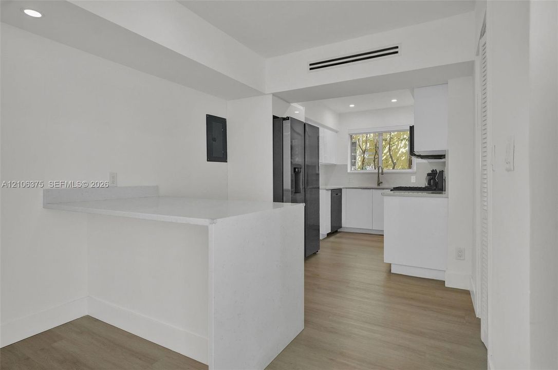 Kitchen featuring crisp white cabinetry, light-toned wood-finish flooring, recessed lighting, and a solid-surface peninsula countertop