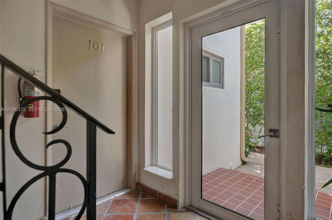 Entryway featuring terracotta-style tile flooring, a glass-panel exterior door, a vertical sidelight window, and decorative wrought-iron railings