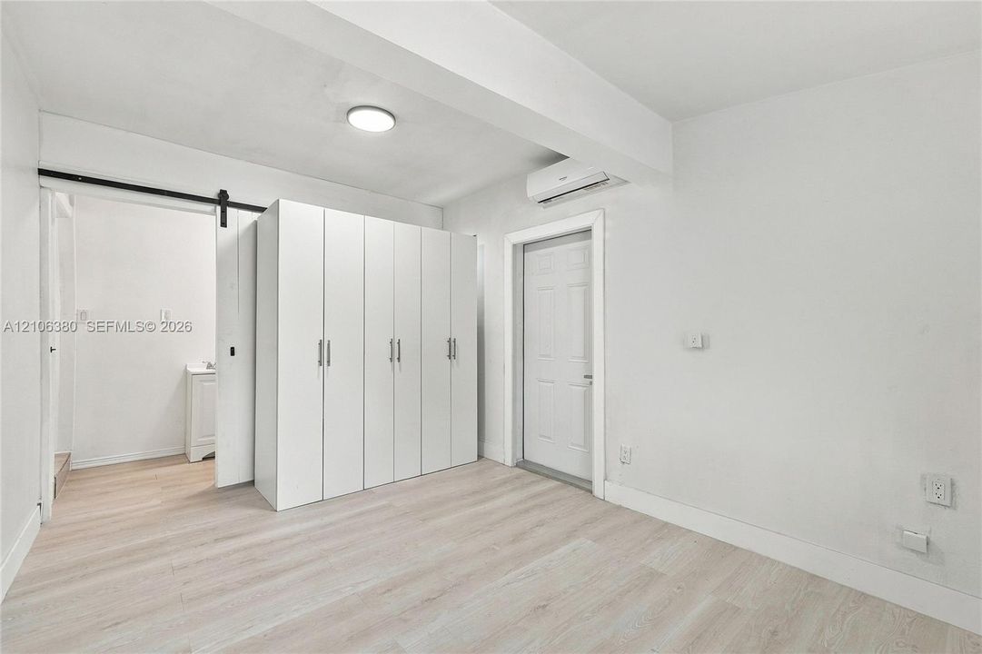 Interior space featuring light-toned wood-finish flooring, white built-in cabinetry, a sliding barn-style door, and a wall-mounted climate control unit