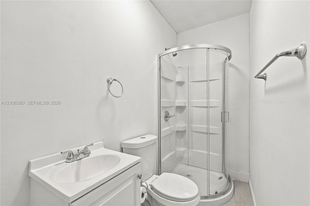 Bathroom featuring a corner shower enclosure with a molded surround, white pedestal vanity with dual-handle faucet, and chrome hardware throughout