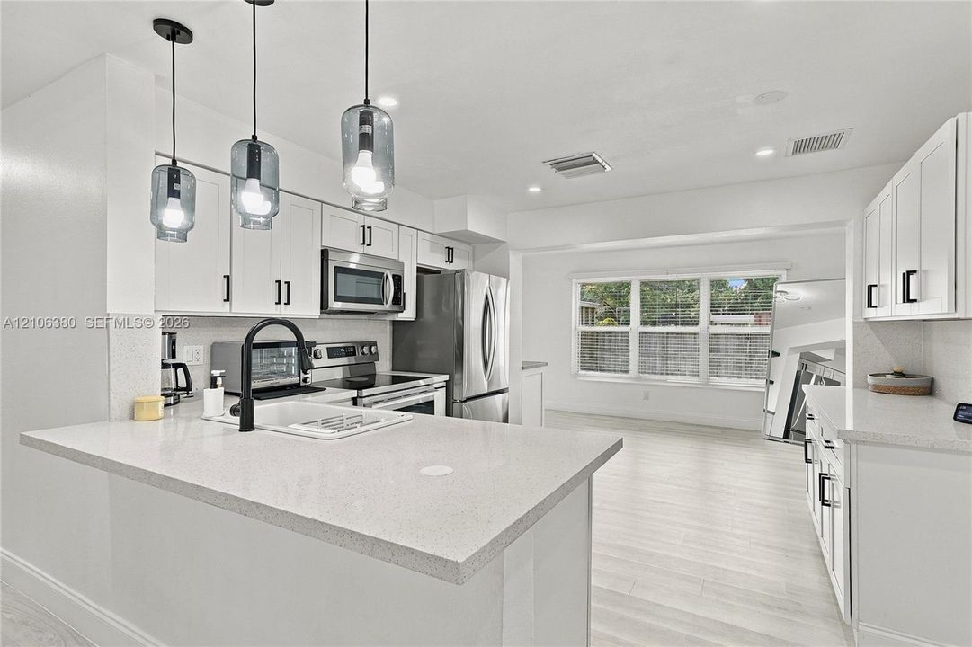 Kitchen featuring white cabinetry, solid-surface countertops, stainless steel appliances, a farmhouse-style sink with a matte black faucet, and glass pendant lighting